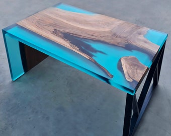 Puede incluir: Una mesa de centro con una tapa de madera y una incrustación de resina epoxi turquesa. La mesa tiene un marco de metal negro.