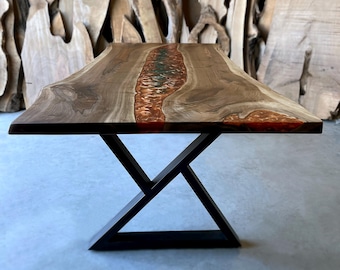 May include: A wooden dining table with a live edge top and a black metal X-shaped base. The table top features a resin river with green and orange accents.