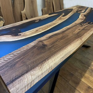 Puede incluir: Una mesa de madera con un r&iacute;o de resina epoxi azul que la atraviesa. La madera tiene un veteado natural y la resina es lisa y brillante.