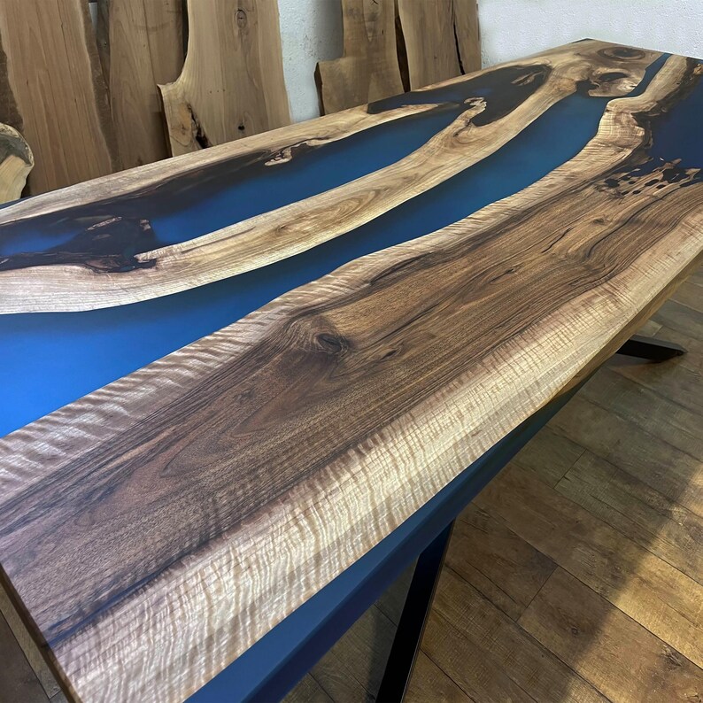 Puede incluir: Una mesa de madera con un r&iacute;o de resina epoxi azul que la atraviesa. La madera tiene un veteado natural y la resina es lisa y brillante.