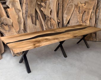 May include: A long wooden dining table with a black epoxy river running down the center. The table is supported by two black metal X-shaped legs.