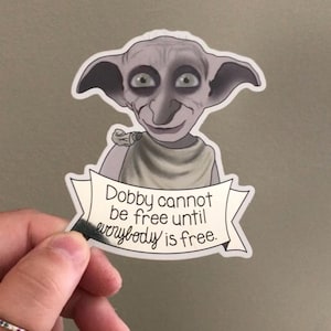 May include: A sticker featuring Dobby, a character from the Harry Potter series, with large ears and wide eyes. The sticker has a banner with the text "Dobby cannot be free until everybody is free."