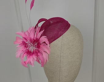 May include: A pink and fuchsia hat with a pink feather flower accent. The hat is on a mannequin head.