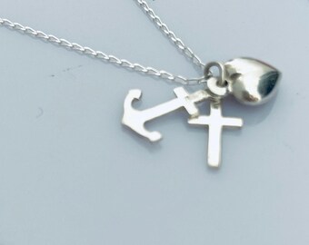 May include: A silver necklace with three charms: a heart, an anchor, and a cross.