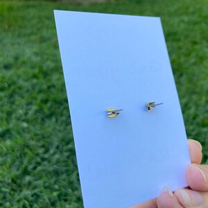 K&ouml;nnte beinhalten: Ein Paar silberne Ohrstecker mit einem kleinen, klaren Stein in der Mitte. Die Ohrringe befinden sich auf einer wei&szlig;en Karte.
