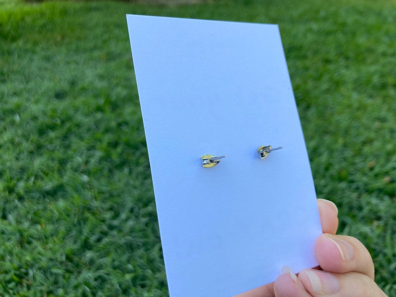 K&ouml;nnte beinhalten: Ein Paar silberne Ohrstecker mit einem kleinen, klaren Stein in der Mitte. Die Ohrringe befinden sich auf einer wei&szlig;en Karte.