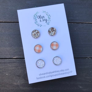 Op de afbeelding: Een set van zes oorbel studs gepresenteerd op een witte kaart met de tekst "Olive & Ivy" en contactgegevens. De oorbel studs hebben verschillende ontwerpen, waaronder glitter, gingham en strass.