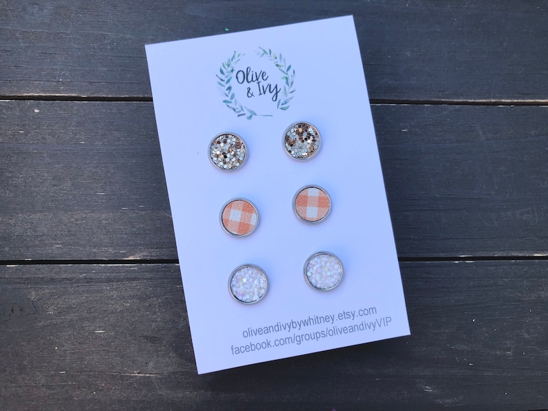 Op de afbeelding: Een set van zes oorbel studs gepresenteerd op een witte kaart met de tekst "Olive & Ivy" en contactgegevens. De oorbel studs hebben verschillende ontwerpen, waaronder glitter, gingham en strass.