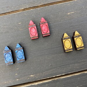 K&ouml;nnte beinhalten: Sechs Ohrringe in Form von Holzstiften. Zwei sind rot mit Glitzer, zwei sind blau mit Glitzer und zwei sind gelb mit Glitzer.