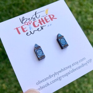K&ouml;nnte beinhalten: Ein Paar blaue Glitzer-Kreide-Ohrringe mit dem Text "Best Teacher Ever" auf einer wei&szlig;en Karte.
