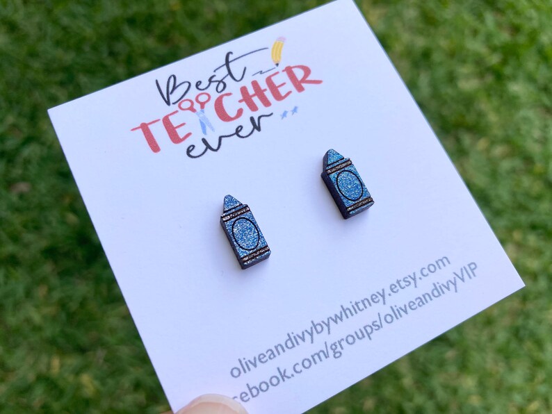 K&ouml;nnte beinhalten: Ein Paar blaue Glitzer-Kreide-Ohrringe mit dem Text "Best Teacher Ever" auf einer wei&szlig;en Karte.