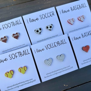 May include: A collection of heart-shaped earrings on white cards, each featuring a different sports theme: football, soccer, baseball, softball, volleyball, and basketball. The text "I love" precedes each sport's name.