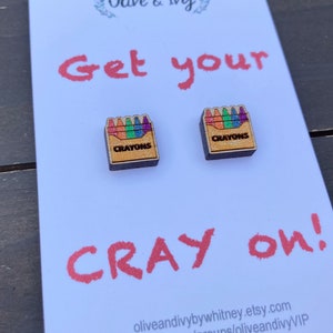 K&ouml;nnte beinhalten: Eine wei&szlig;e Karte mit dem Text "Get your Cray on!" und zwei kleine Holzkisten mit dem Wort "Crayons" und einem Regenbogen aus Buntstiften darauf.