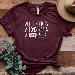 May include: Burgundy t-shirt with white text that reads "All I need is a long nap & a good book".