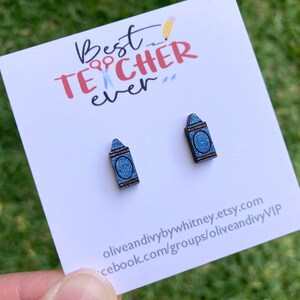 K&ouml;nnte beinhalten: Ein Paar blaue Glitzer-Kreide-Ohrringe mit dem Text "Best Teacher Ever" auf einer wei&szlig;en Karte.