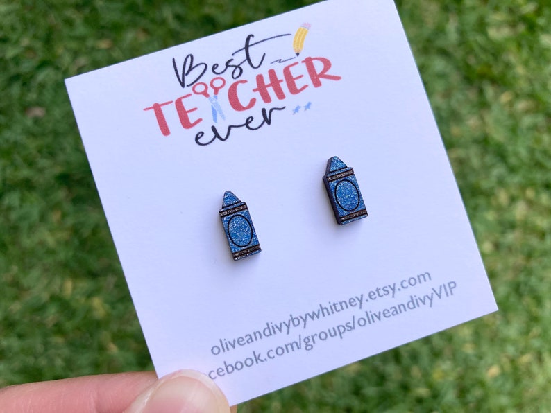 K&ouml;nnte beinhalten: Ein Paar blaue Glitzer-Kreide-Ohrringe mit dem Text "Best Teacher Ever" auf einer wei&szlig;en Karte.