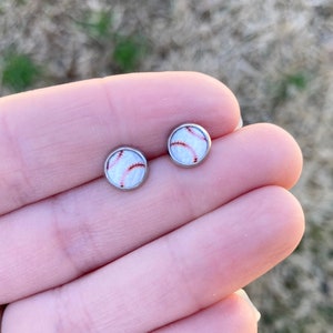 May include: A pair of silver stud earrings with a white baseball design.