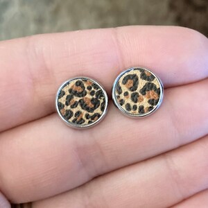 May include: A pair of silver stud earrings with a round, brown, black, and tan leopard print design.