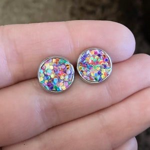 May include: A pair of silver stud earrings with a colorful confetti design. The confetti is a mix of pink, purple, blue, green, yellow, and orange.