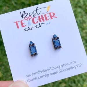 K&ouml;nnte beinhalten: Ein Paar blaue Glitzer-Kreidonstecker. Die Ohrringe befinden sich auf einer wei&szlig;en Karte mit dem Text "Best Teacher Ever" in rosa und roten Buchstaben.