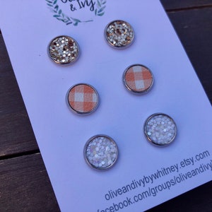 Op de afbeelding: Zes verschillende ronde, zilveromrande, decoratieve versieringen. De versieringen zijn gemaakt van glitter, stof en wit iriserend materiaal. De versieringen worden getoond op een witte kaart met de tekst "oliveandiivybywhitney.etsy.com facebook.com/groups/oliveandiivyVIP".