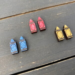 K&ouml;nnte beinhalten: Ein Set mit sechs Holz-Kreide-Ohrringen. Zwei rote, zwei blaue und zwei gelbe Kreiden mit Glitzer.