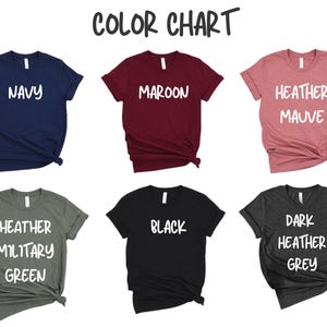 May include: Color chart showing six different t-shirt colors: navy, maroon, heather mauve, heather military green, black, and dark heather grey. Each t-shirt has a different color name printed on it in white.