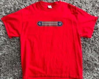 May include: Red t-shirt with a graphic of a skateboard with an American flag design and the text "King of  Deck" on it.