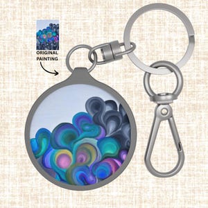 May include: A round keychain with a silver-colored metal frame and hardware. The keychain features an abstract painting with blue, purple, teal, and yellow swirls. The words "ORIGINAL PAINTING" are printed on the image.
