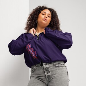 May include: A dark purple windbreaker jacket with a half-zip closure and a drawstring hem. The jacket features a colorful abstract design on the front. The model is wearing the jacket with gray jeans.