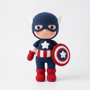 May include: A handmade crochet Captain America doll. The doll is primarily navy blue, red, and white, with a shield and a star on the chest. The doll has a helmet with white wings and a mask.