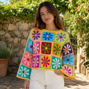 Pode incluir: Um suéter de crochê de manga comprida com um design de retalhos de motivos quadrados. Cada quadrado exibe um padrão floral multicolorido em tons vibrantes de vermelho, azul, amarelo, verde, roxo e rosa, com uma borda amarela.
