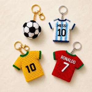 May include: Four crochet keychains including a black and white football, a white and light blue striped jersey with MESSI 10, a yellow jersey with green trim and the number 10, and a red jersey with green trim featuring RONALDO 7.
