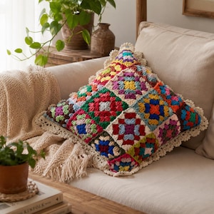 May include: A square throw pillow featuring a colorful granny square crochet pattern with vibrant red, blue, yellow, green, and purple yarn. The pillow is finished with a decorative cream-colored crocheted scalloped edge border.