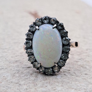 May include: A silver ring with a large oval opal gemstone surrounded by a halo of smaller black gemstones.