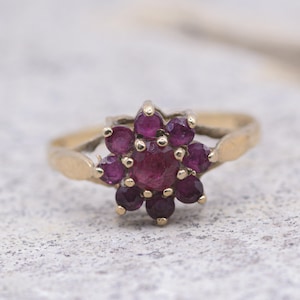 May include: A gold ring with a cluster of purple gemstones set in a flower shape.