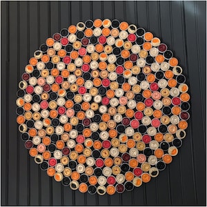 Puede incluir: Una disposición circular de pequeños contenedores redondos y coloridos, que se asemeja a un mandala. Los contenedores son en tonos de naranja, rojo, negro y blanco, creando un patrón vibrante y simétrico.