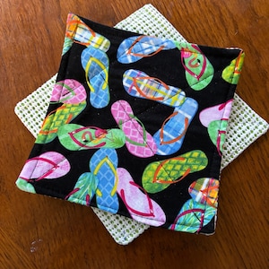 May include: A black square pot holder with a pattern of colorful flip flops on a white background. The pot holder is layered on top of a green and white square pot holder.