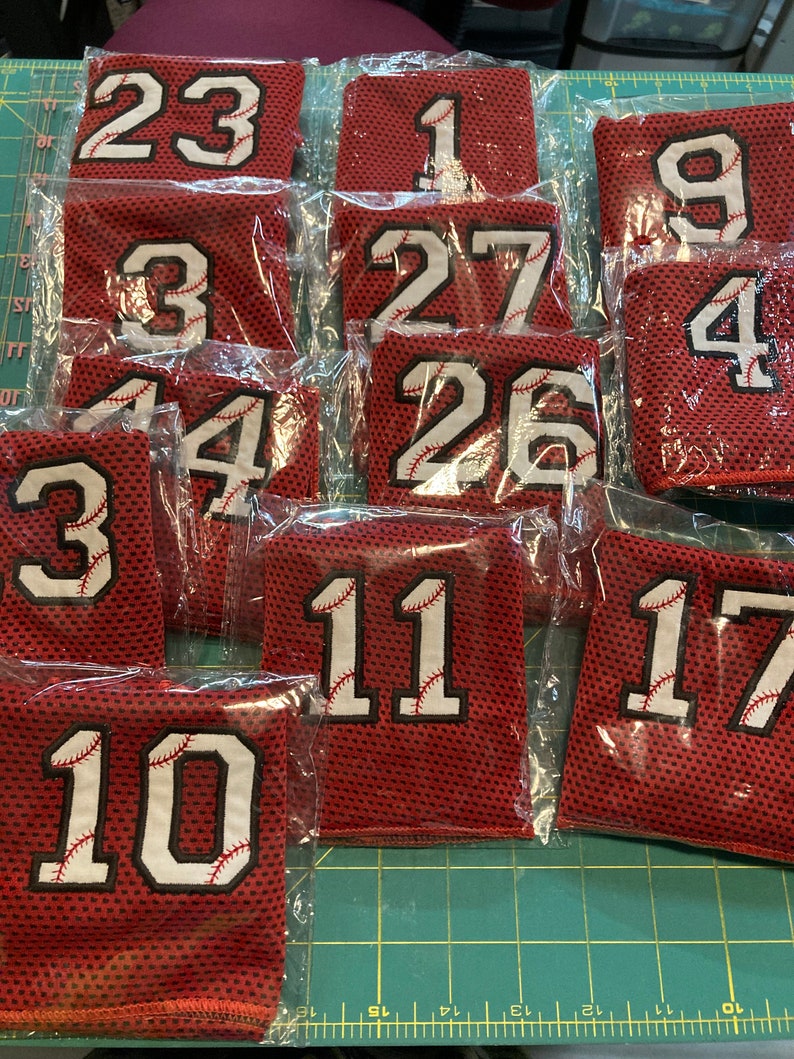 May include: A collection of red mesh fabric patches with white numbers and baseball stitching. Numbers include 23, 1, 9, 4, 3, 27, 26, 11, 17, and 10. Each patch is individually packaged in clear plastic.