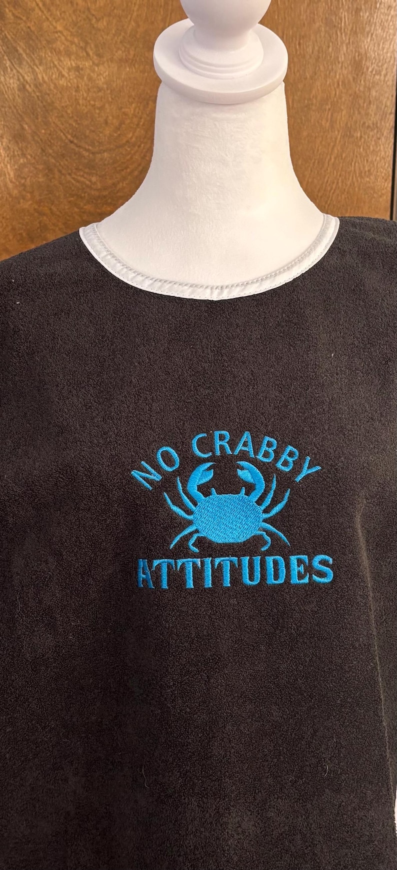May include: Dark gray t-shirt with a white collar and the embroidered phrase "NO CRABBY ATTITUDES" in turquoise. The design includes a turquoise crab graphic.