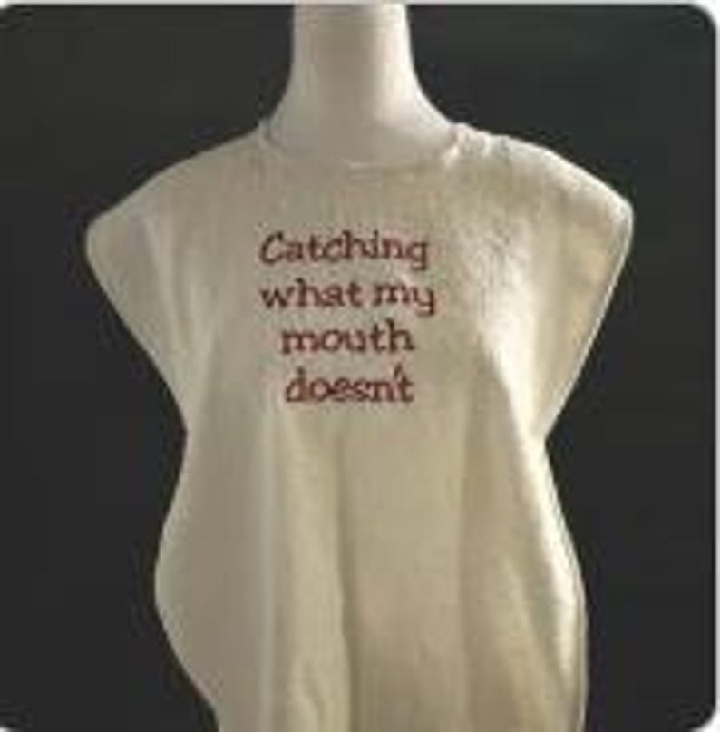 May include: Cream-colored sleeveless shirt with the embroidered text "Catching what my mouth doesn't" in a dark red color. The shirt is displayed on a mannequin against a dark background.