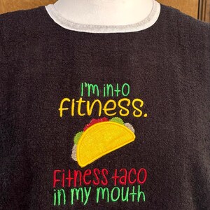 May include: Black embroidered sweatshirt with the text "I'm into fitness. Fitness taco in my mouth." The design includes a yellow taco with green, red, and white details. The sweatshirt has a white trim around the neckline.