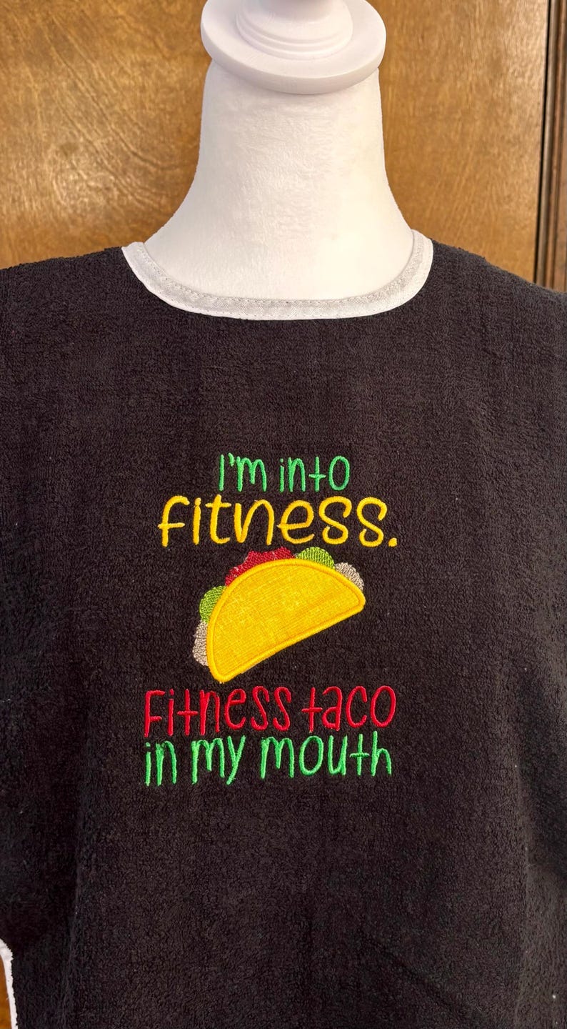 May include: Black embroidered sweatshirt with the text "I'm into fitness. Fitness taco in my mouth." The design includes a yellow taco with green, red, and white details. The sweatshirt has a white trim around the neckline.