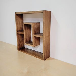 May include: A wooden wall shelf with a square design and multiple compartments. The shelf is made of dark brown wood and has a rustic look.