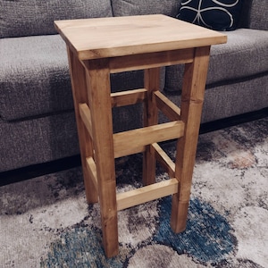 May include: A wooden stool with a natural finish and a simple design. The stool has three shelves and is made of solid wood.
