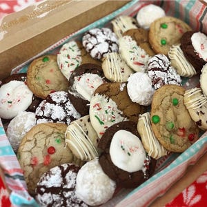 Può includere: Una scatola piena di biscotti assortiti. I biscotti sono di varie forme e dimensioni, con diversi condimenti come zuccherini, zucchero a velo e cioccolato bianco. Alcuni biscotti hanno caramelle rosse e verdi.