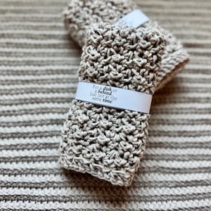 May include: Two beige crocheted dishcloths with a white label that reads "For a dish or a behind, just not at the same time!"