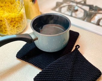May include: A blue speckled pot with a black handle sits on two black knitted pot holders. The pot is filled with water and steam is rising from it.