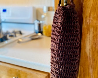 May include: A brown crocheted bag hanging on a cabinet door handle in a kitchen. The bag is made of a textured, open weave material.