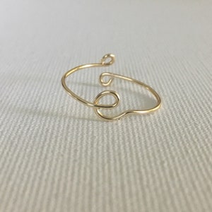 Puede incluir: Un brazalete de alambre dorado con un diseño simple y abstracto.